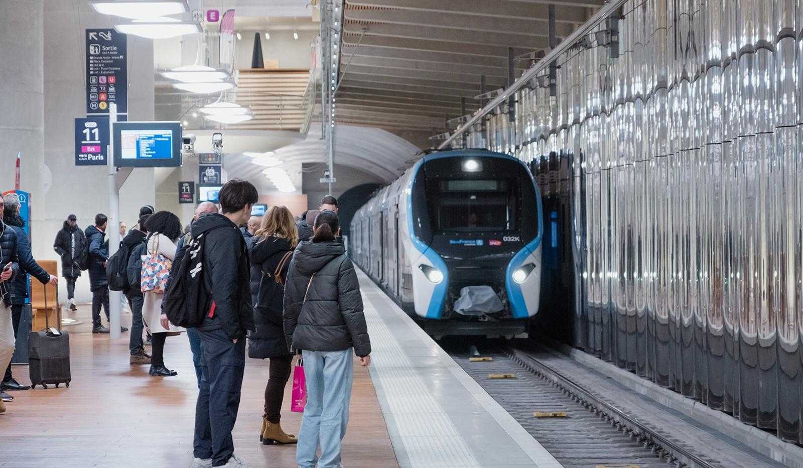 Sur le quai d'un tunnel, des voyageurs debouts  attendent leur train qui arrive en gare 