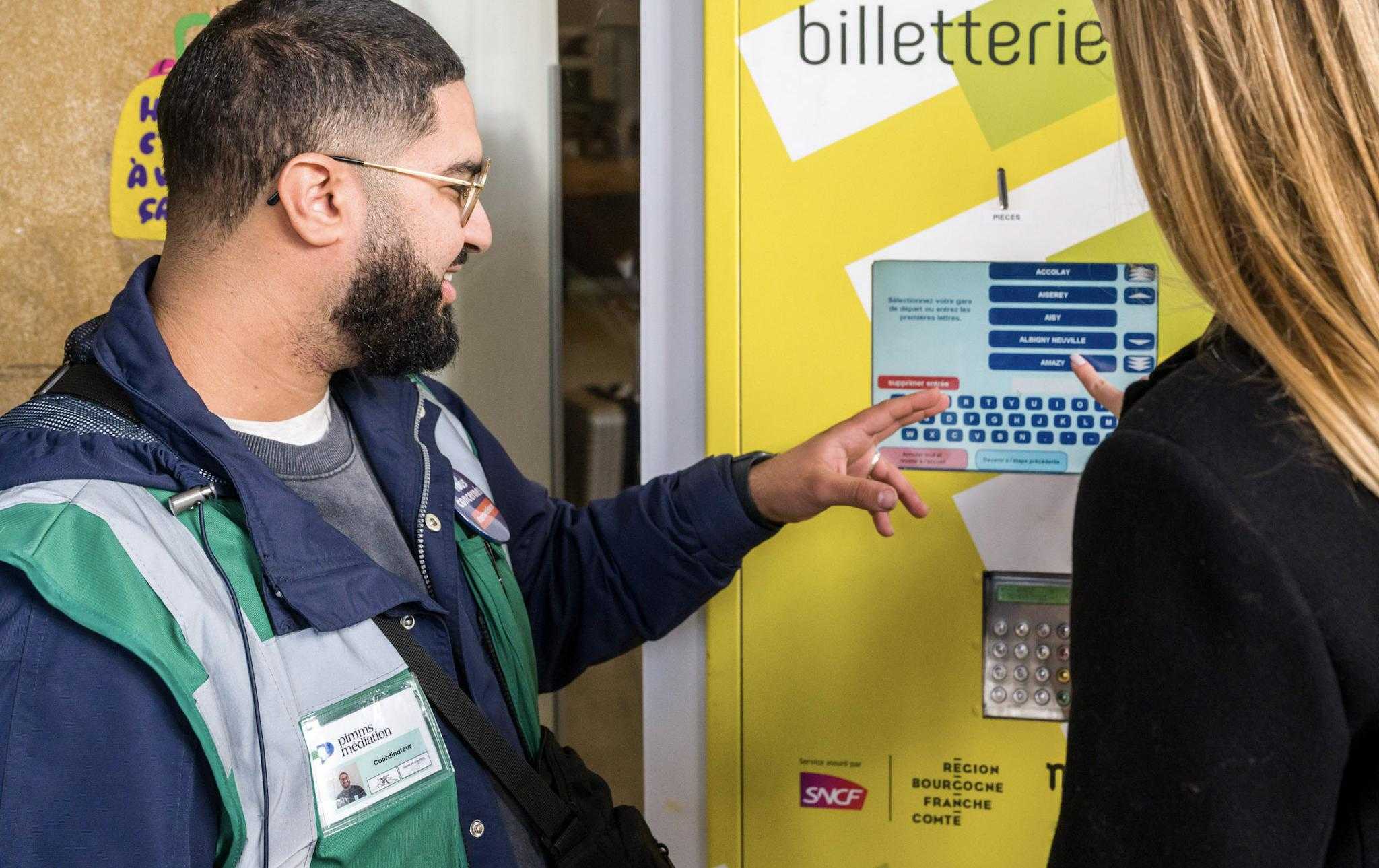 Un médiateur PIMMS Point d'Information Médiation Multiservices aide un voyageur à l'achat de titres de transport sur un automate de vente
